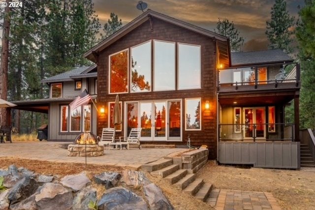 back house at dusk featuring a balcony, an outdoor fire pit, and a patio area