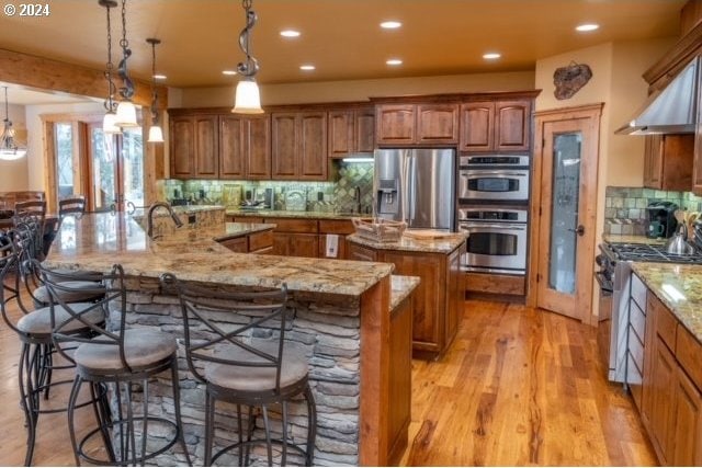 kitchen with decorative backsplash, stainless steel appliances, light hardwood / wood-style floors, and hanging light fixtures