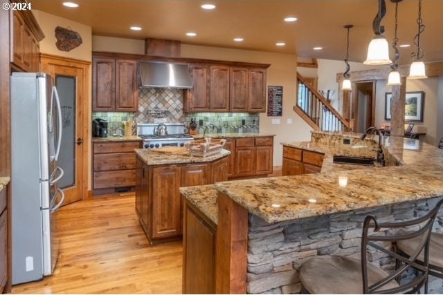 kitchen featuring sink, decorative light fixtures, a large island with sink, stainless steel appliances, and light hardwood / wood-style floors