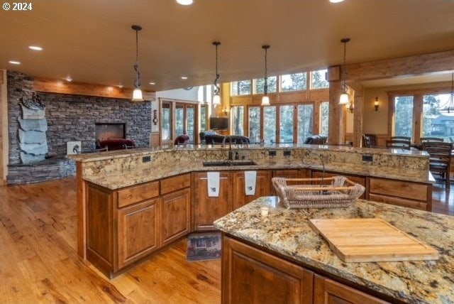 kitchen featuring hanging light fixtures, light hardwood / wood-style floors, a stone fireplace, light stone countertops, and sink