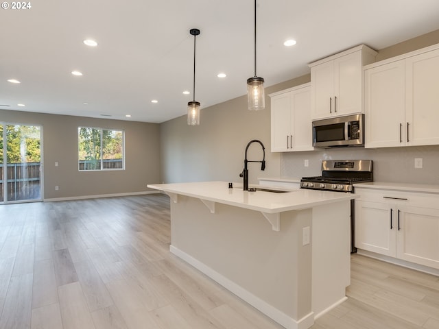 kitchen with a center island with sink, a sink, light countertops, light wood-style floors, and appliances with stainless steel finishes