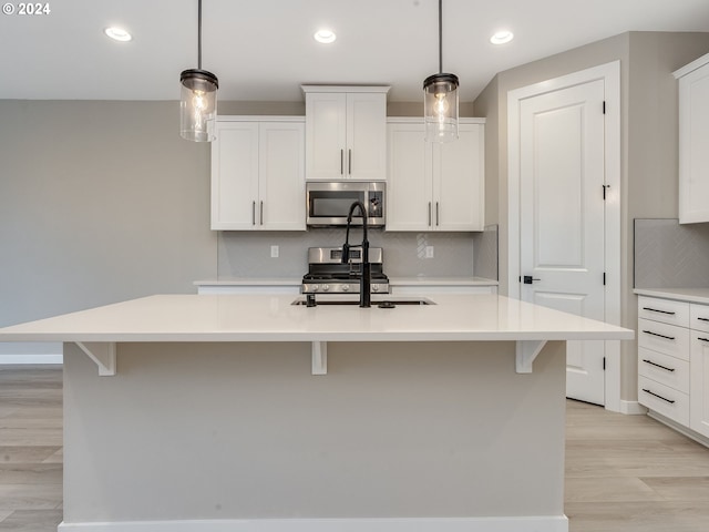 kitchen with an island with sink, pendant lighting, light hardwood / wood-style flooring, and appliances with stainless steel finishes