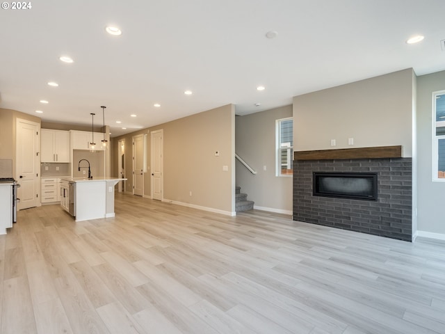 unfurnished living room featuring a glass covered fireplace, recessed lighting, stairway, light wood finished floors, and baseboards