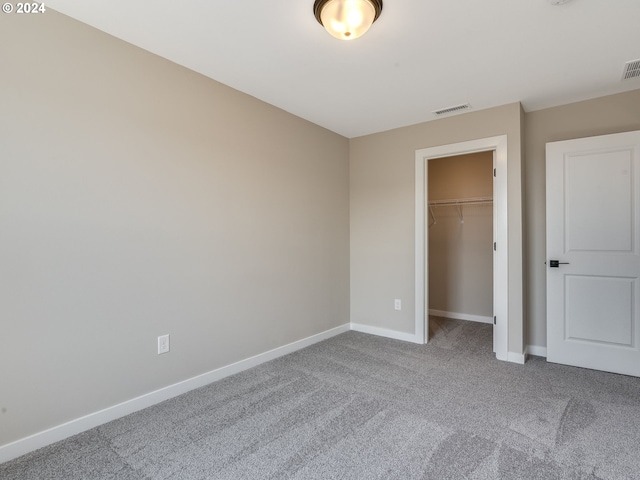 unfurnished bedroom with visible vents, baseboards, a walk in closet, and carpet flooring