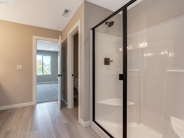 bathroom with a shower with shower door, toilet, and wood-type flooring