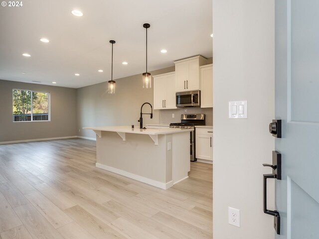 kitchen with stainless steel appliances, light hardwood / wood-style floors, white cabinetry, pendant lighting, and a center island with sink