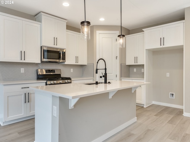 kitchen featuring a sink, a kitchen island with sink, light wood finished floors, and stainless steel appliances