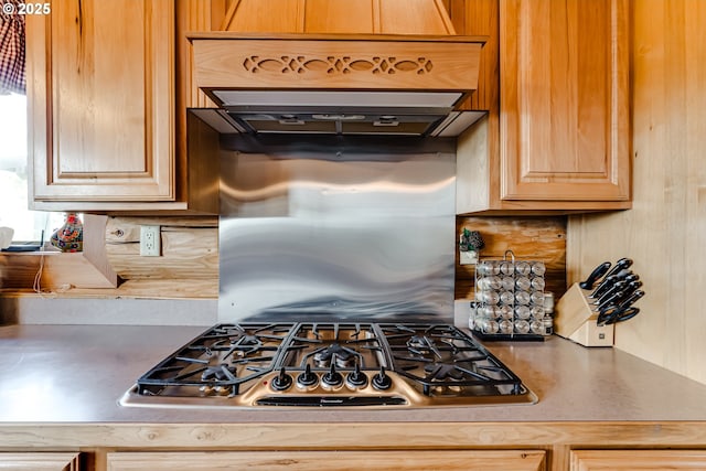 kitchen with premium range hood, stainless steel gas stovetop, light brown cabinets, and backsplash