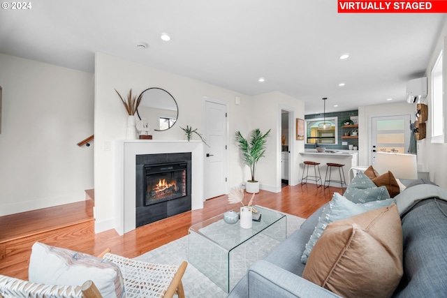 living room with an AC wall unit, light wood-type flooring, and a fireplace