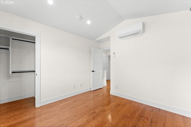 unfurnished bedroom featuring lofted ceiling, a wall mounted air conditioner, light wood-type flooring, and a closet