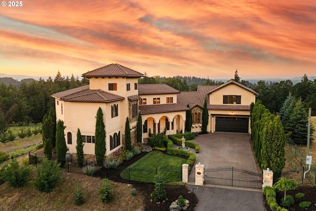 mediterranean / spanish home featuring a fenced front yard, a tile roof, decorative driveway, a gate, and stucco siding