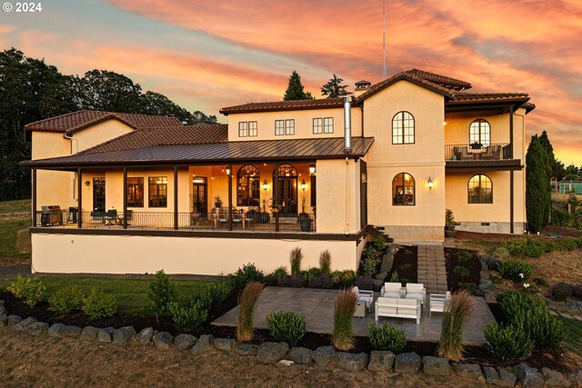 4974 W 44th Ave, Eugene, OR 97405 - back of house at dusk featuring a balcony, stucco siding, a standing seam roof, a patio, and metal roof