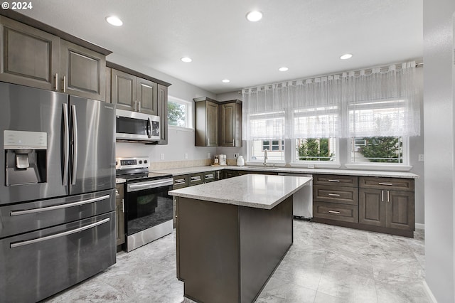 kitchen with a center island, sink, appliances with stainless steel finishes, dark brown cabinets, and light stone counters