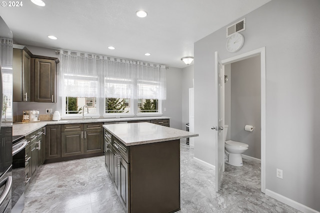 kitchen featuring a center island, stove, dark brown cabinetry, and sink