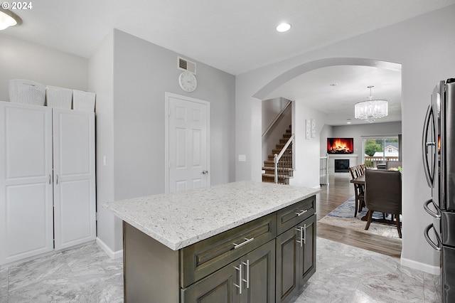 kitchen with a center island, an inviting chandelier, decorative light fixtures, dark brown cabinetry, and stainless steel refrigerator