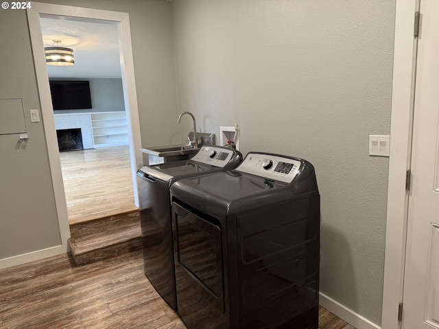 clothes washing area with a fireplace, dark hardwood / wood-style floors, washer and clothes dryer, and sink