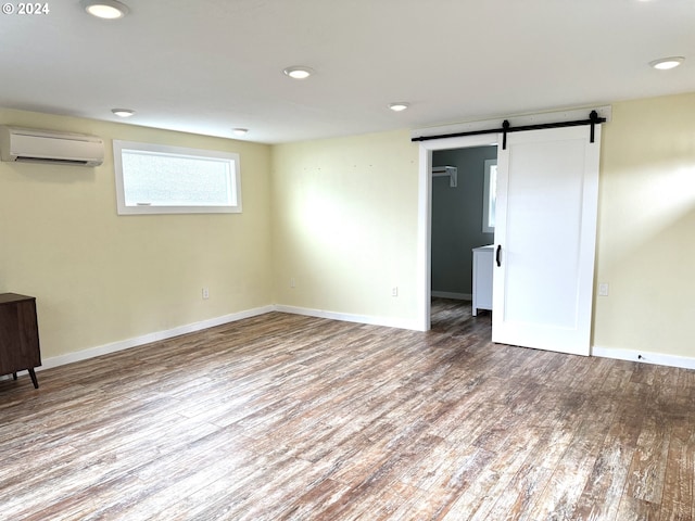 unfurnished room with wood-type flooring, a barn door, and a wall unit AC