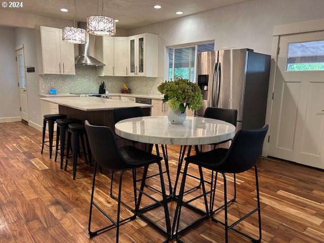 kitchen with white cabinetry, hardwood / wood-style flooring, wall chimney exhaust hood, and stainless steel fridge with ice dispenser