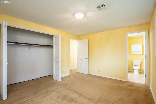 unfurnished bedroom with light colored carpet, connected bathroom, a closet, and a textured ceiling