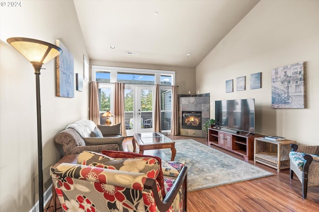 living room featuring hardwood / wood-style floors, high vaulted ceiling, and a tile fireplace