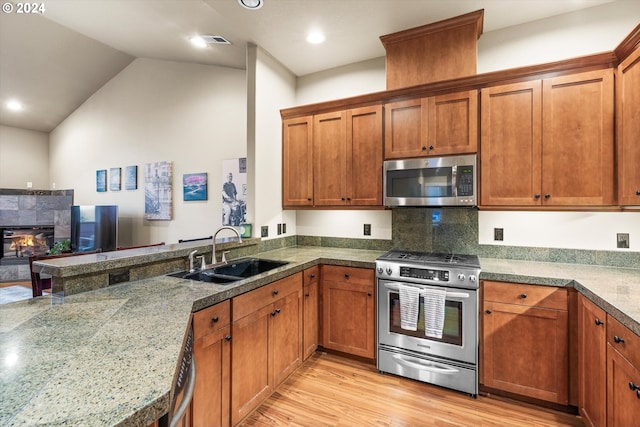 kitchen with stainless steel appliances, light wood-type flooring, sink, lofted ceiling, and a tile fireplace