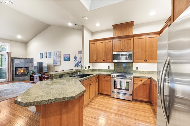 kitchen with kitchen peninsula, sink, a fireplace, light wood-type flooring, and appliances with stainless steel finishes