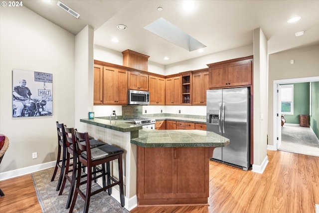 kitchen with stainless steel appliances, light wood-type flooring, kitchen peninsula, a breakfast bar, and a skylight