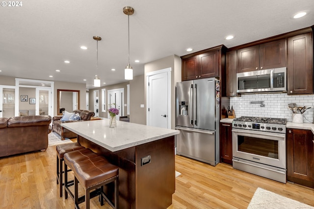 kitchen with decorative backsplash, dark brown cabinets, pendant lighting, and stainless steel appliances