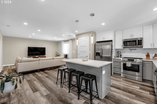 kitchen with white cabinets, a center island, decorative light fixtures, stainless steel appliances, and a breakfast bar