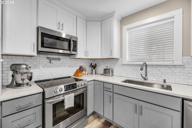 kitchen with sink, light wood-type flooring, gray cabinets, decorative backsplash, and stainless steel appliances