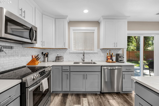 kitchen with gray cabinetry, sink, dark wood-type flooring, backsplash, and stainless steel appliances