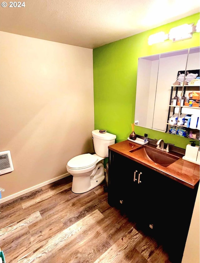 bathroom with toilet, heating unit, wood finished floors, and vanity