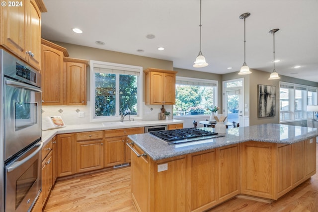 kitchen with light hardwood / wood-style floors, sink, hanging light fixtures, a kitchen island, and stainless steel appliances