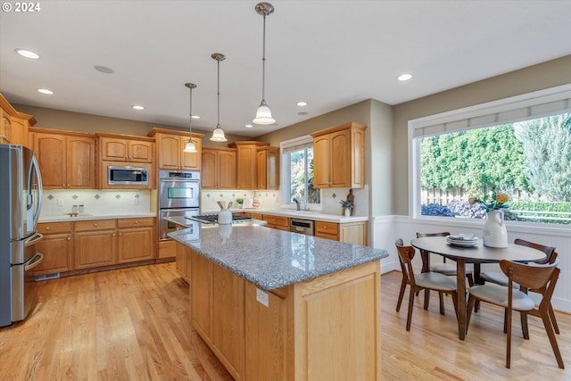 kitchen with light hardwood / wood-style floors, hanging light fixtures, a kitchen island, stainless steel appliances, and light stone countertops