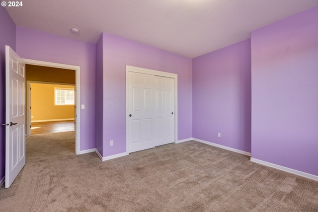 unfurnished bedroom featuring a textured ceiling, light colored carpet, and a closet