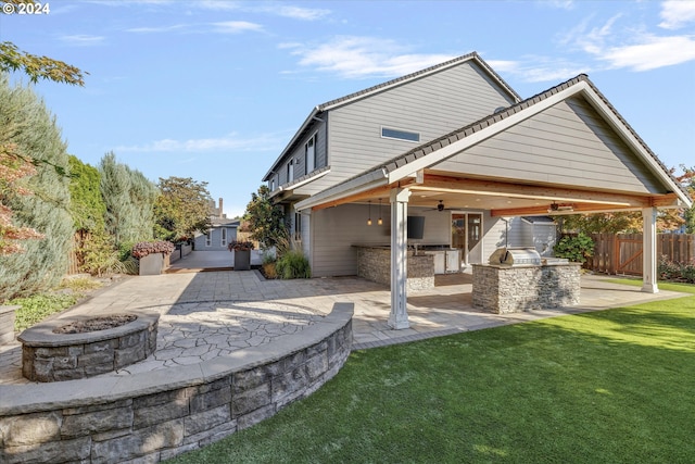 rear view of property featuring exterior kitchen, a patio area, an outdoor fire pit, ceiling fan, and a yard