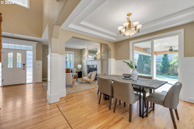 dining room featuring ceiling fan with notable chandelier, light hardwood / wood-style floors, a raised ceiling, and plenty of natural light