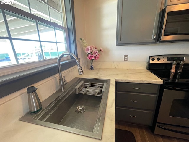 kitchen featuring wood finished floors, stainless steel appliances, light stone counters, and a sink