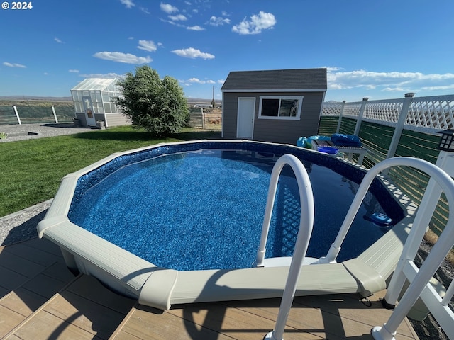 view of pool with an outbuilding, fence, and a greenhouse