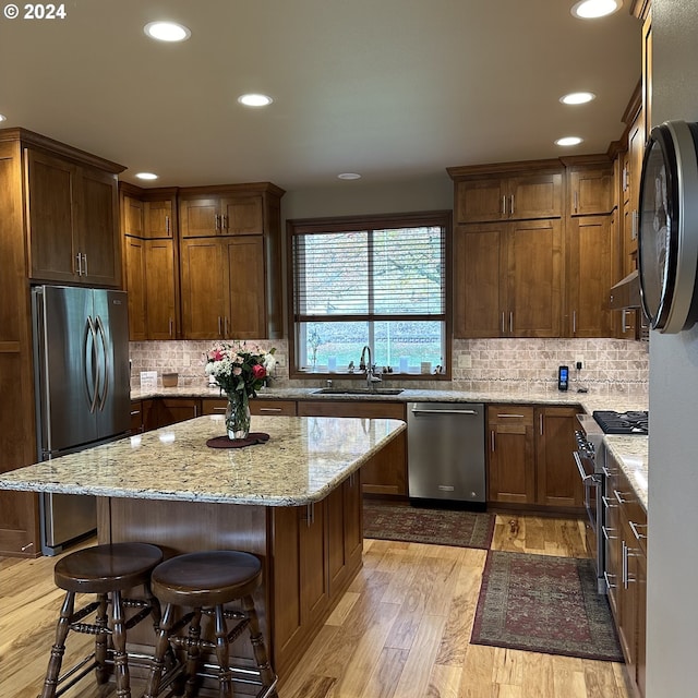 kitchen featuring stainless steel appliances, sink, light hardwood / wood-style flooring, a kitchen island, and a breakfast bar area