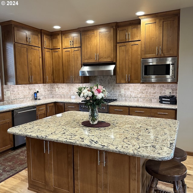 kitchen featuring light stone counters, light hardwood / wood-style floors, a kitchen bar, decorative backsplash, and appliances with stainless steel finishes