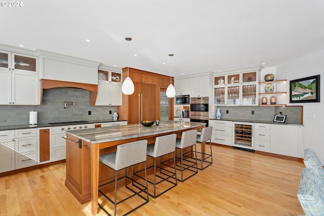 kitchen featuring pendant lighting, a breakfast bar, appliances with stainless steel finishes, a kitchen island with sink, and beverage cooler