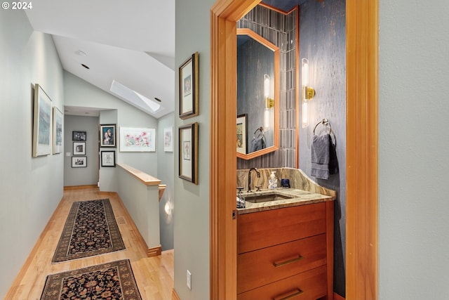 hall with lofted ceiling, light hardwood / wood-style floors, and sink