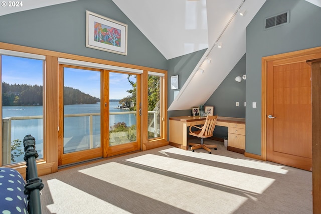 carpeted home office with a water view, track lighting, built in desk, and high vaulted ceiling