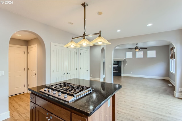 kitchen featuring stainless steel gas stovetop, dark stone counters, hanging light fixtures, a kitchen island, and light hardwood / wood-style flooring