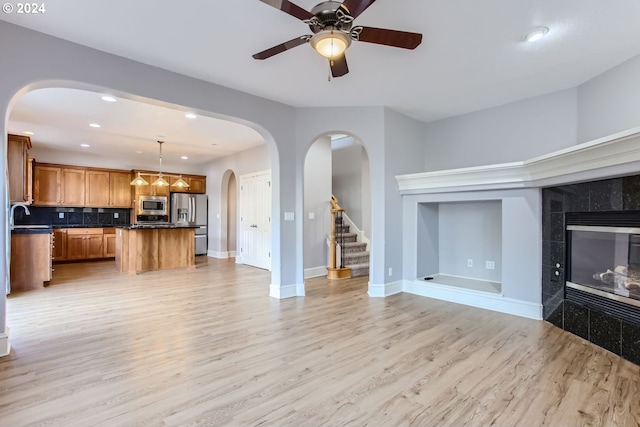 unfurnished living room with a tile fireplace, ceiling fan, and light hardwood / wood-style flooring