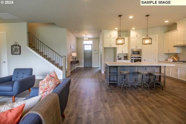 kitchen with pendant lighting, a kitchen island with sink, dark hardwood / wood-style flooring, white cabinetry, and stainless steel appliances