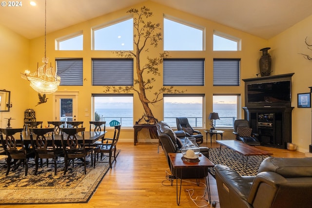 living room featuring plenty of natural light, high vaulted ceiling, light hardwood / wood-style floors, and a notable chandelier