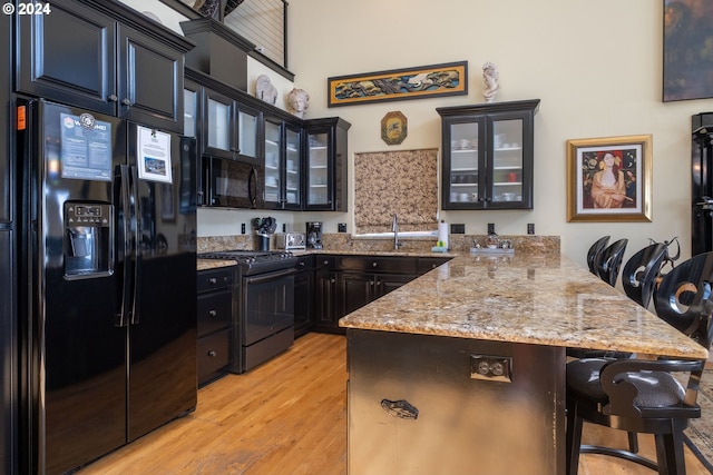 kitchen featuring black appliances, a kitchen breakfast bar, light hardwood / wood-style floors, and light stone countertops