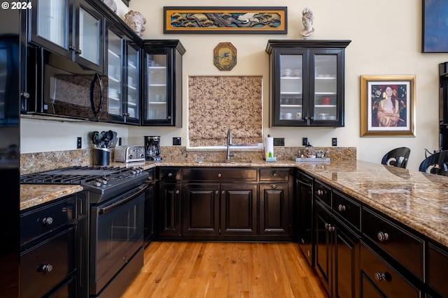 kitchen featuring black appliances, light hardwood / wood-style floors, light stone counters, and sink